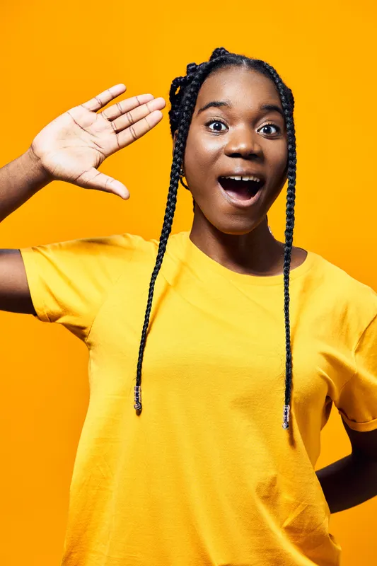 Young Black woman in a bright yellow t shirt expressing joy against a vibrant yellow background, showcasing a cheerful and energetic mood for lifestyle themes