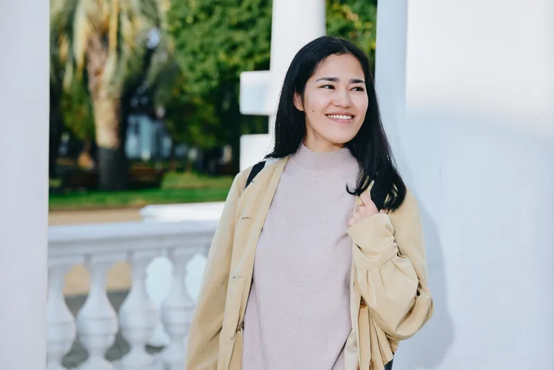 Woman in beige jacket and cozy sweater outdoors, smiling along a sunny veranda, casual fashion and relaxed mood, travel style and everyday elegance