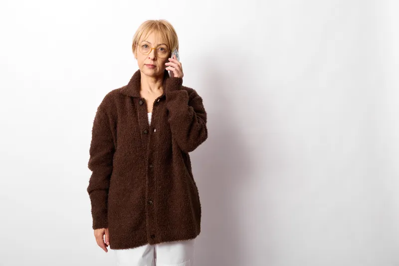 woman elderly portrait studio thinking hand near face calm expression wearing brown coat white background studio shot with copy space soft light indoors quiet mood
