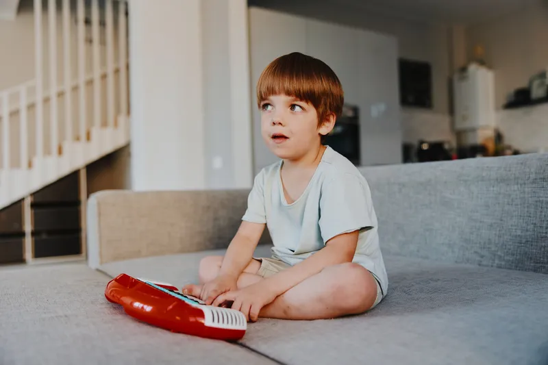 A young boy sitting on a couch, deeply focused while playing a colorful keyboard instrument, showcasing creativity and joy in a cozy home environment.