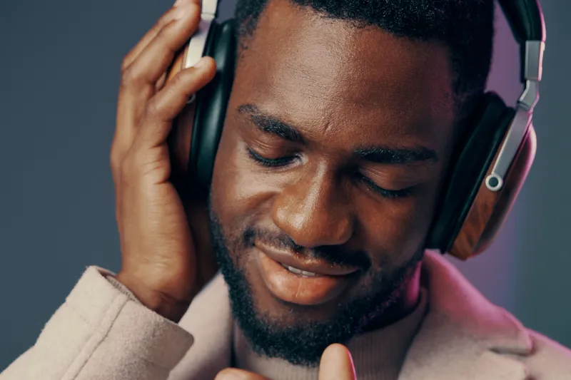 Young Black man enjoying music with headphones, showcasing relaxation and happiness against a colorful background, perfect for lifestyle and wellness concepts
