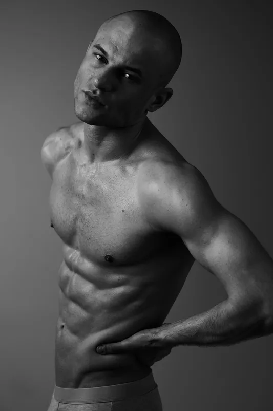 Strong man posing in black and white, showcasing defined muscles and a confident expression, highlighting body artistry and strength.
