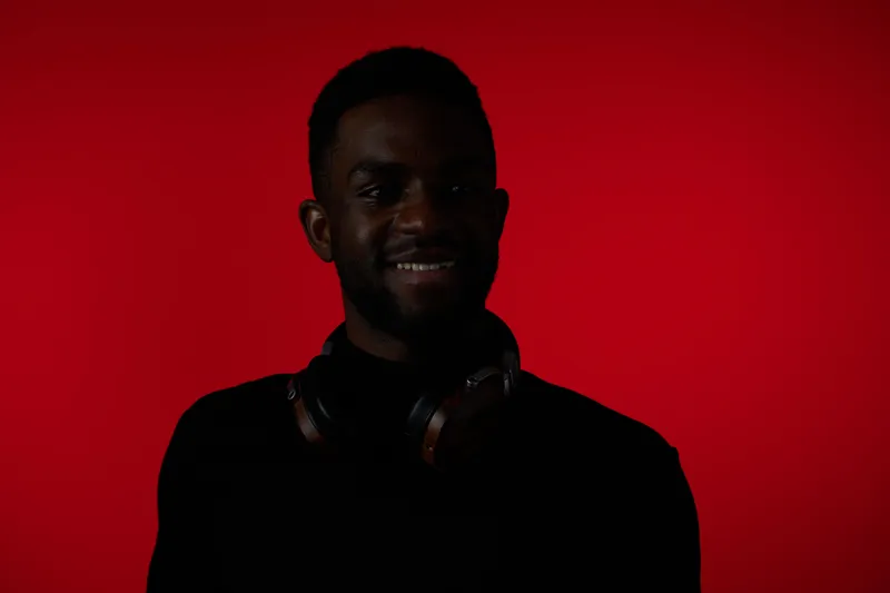 Smiling Black man with headphones on a vibrant red background, showcasing style and confidence, perfect for music, lifestyle, and personal branding concepts