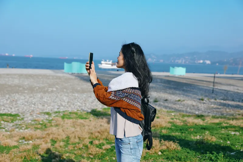 woman selfie phone beach outdoors vacation, candid outdoor shot of a woman taking a photo with smartphone by the shore, sunny day, casual style, scenic horizon and sea breeze
