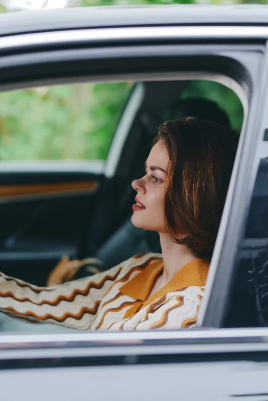 Portrait of a woman sitting in a car, head turned slightly to the side, sunlit profile, calm and thoughtful expression, soft colors.