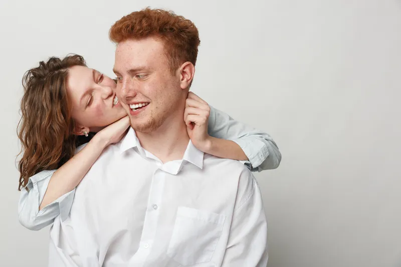 Happy young couple embraces and smiles in casual clothes against white background. Concept of love, affection, relationship, and joyful moments between man and woman.