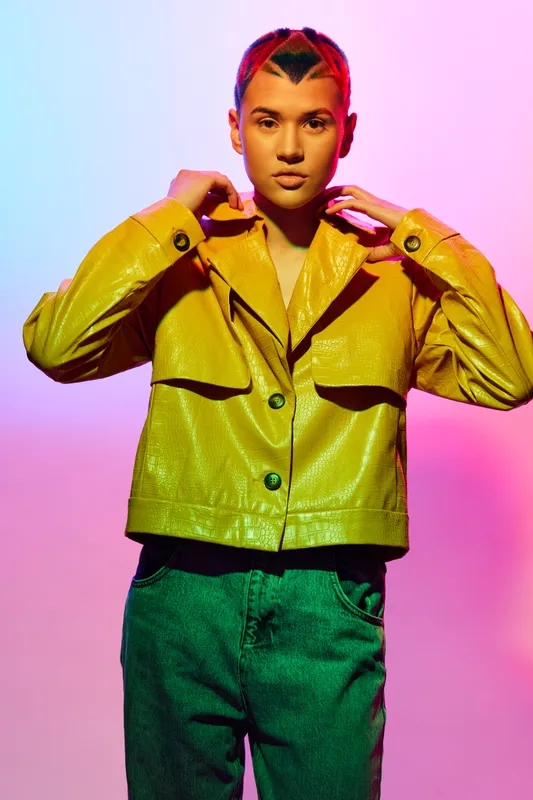stylish woman in yellow jacket and green pants poses confidently with colorful pink and blue gradient background, trendy fashion look, modern youthful style
