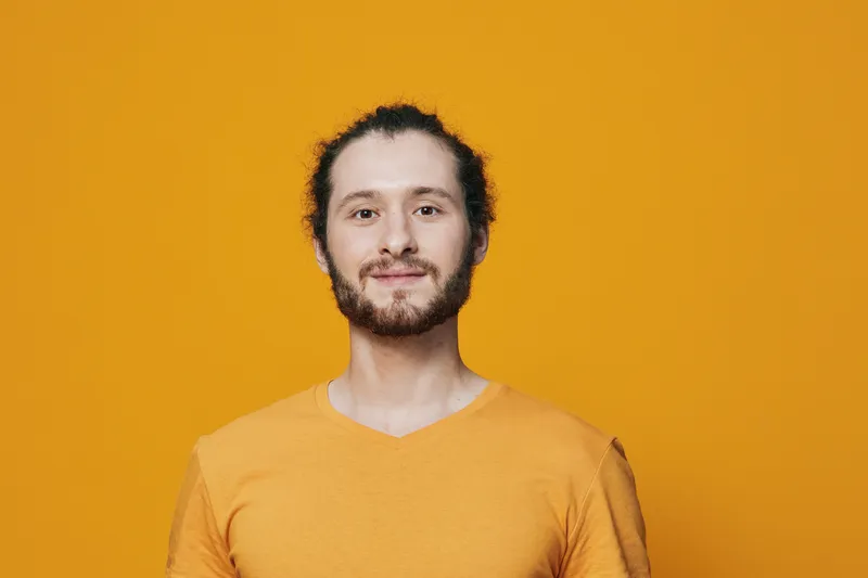 Cheerful young man with curly hair and beard wearing a yellow t shirt against a vibrant yellow background, expressing confidence and happiness