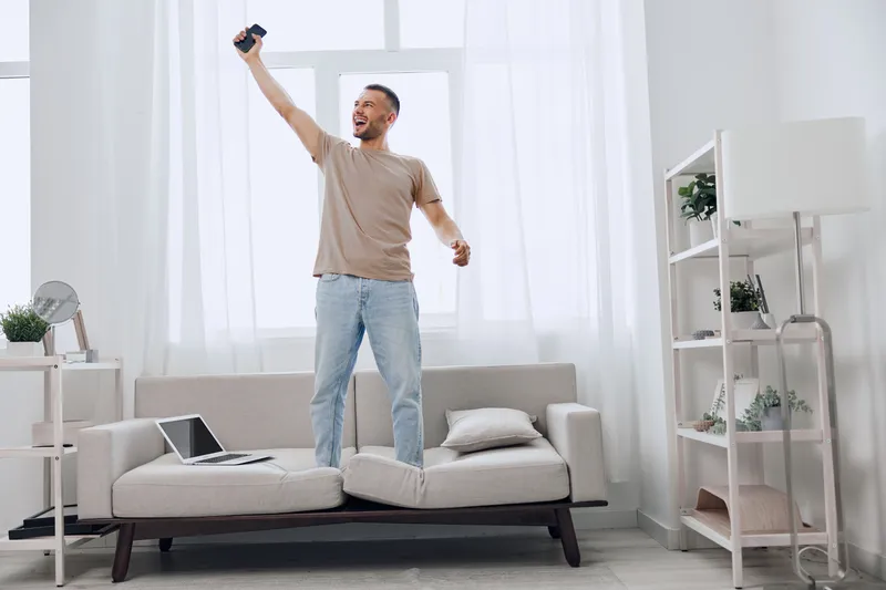 Excited man celebrating while taking a selfie in a bright, modern living room filled with natural light, showcasing joy and a vibrant lifestyle.