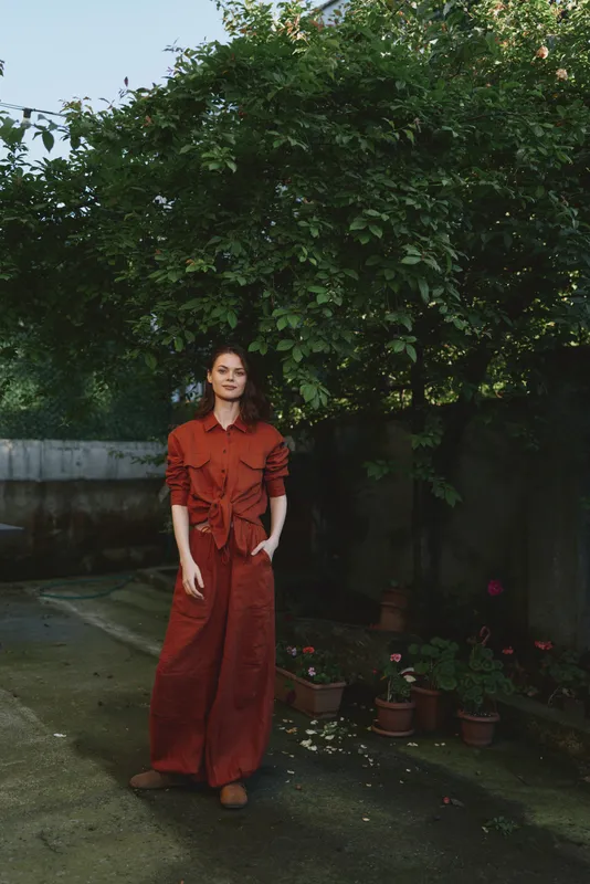 Woman in a red dress standing in a garden, full body shot under natural daylight, lush greenery, relaxed mood, lifestyle portrait with outdoorsy vibe, showcasing everyday style