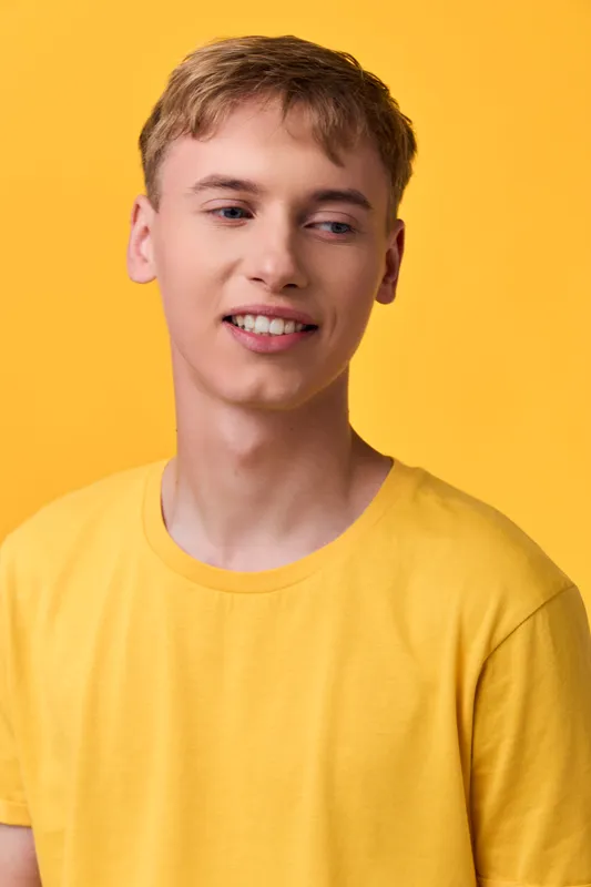 Young man in a bright yellow tee against a vivid yellow backdrop, casual style, relaxed pose, soft smile, studio lighting, modern fashion mood, warm color harmony