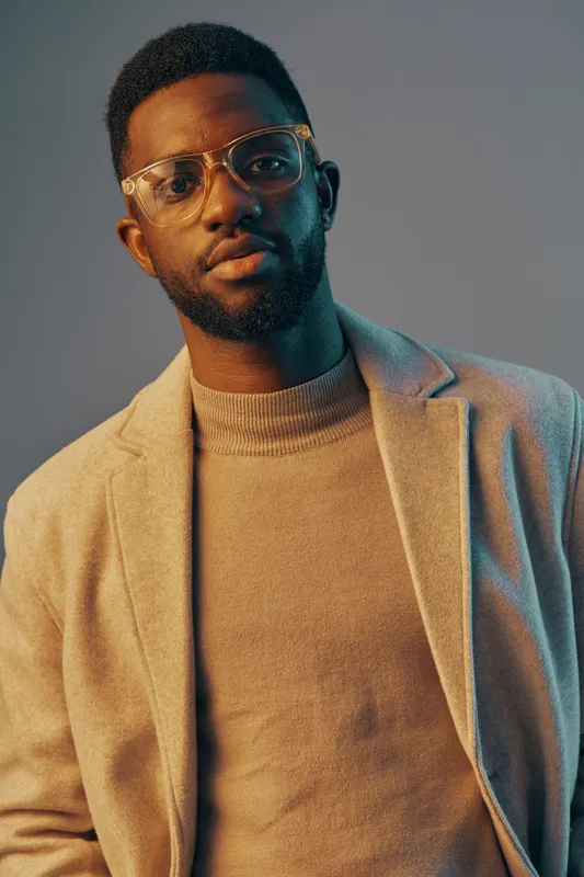 Stylish African man wearing glasses and a light sweater, posing confidently in a modern setting with a blue and orange background