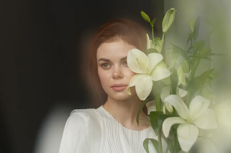 Young woman with a serene expression holding white lilies, capturing a moment of tranquility and beauty in a soft, ethereal setting