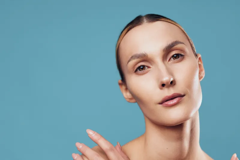 Close-up portrait of a woman with clear skin against a blue backdrop, highlighting beauty and skincare concepts, soft studio lighting creates a calm, confident mood for lifestyle and wellness.
