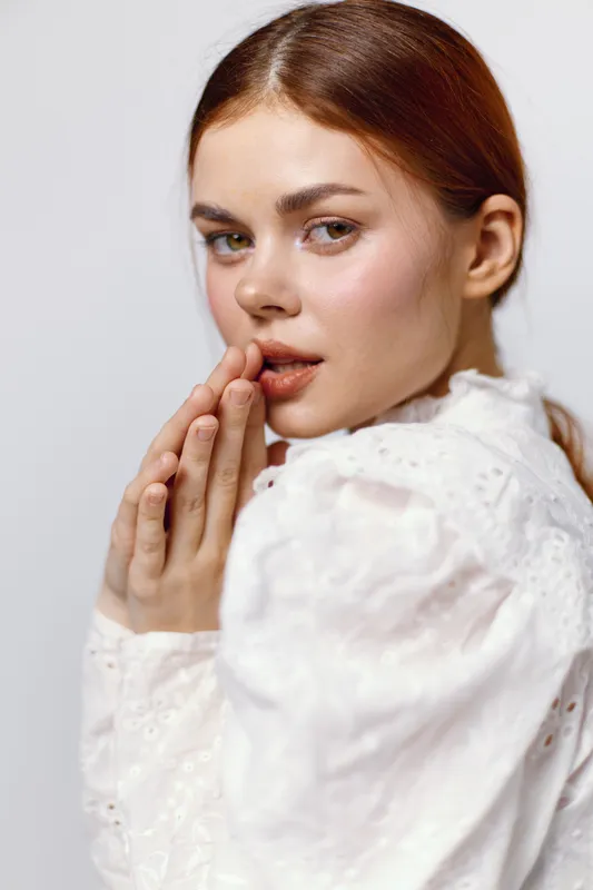Young woman in a white blouse expressing curiosity with a soft gaze and touch of elegance, showcasing seasonal beauty and emotional connection
