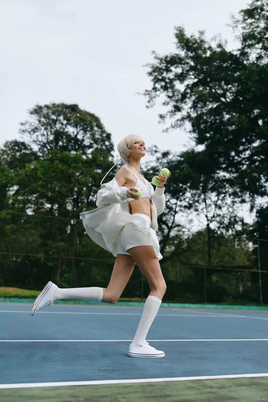 Athletic young model running joyfully on a tennis court, dressed in a white sporty outfit, exuding energy and enthusiasm on a sunny day