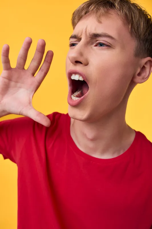 Shouting, boy, open mouth, hand, red shirt, yellow background, expression, energy captured in a bold studio shot with vibrant emotion and dynamic action in a close up
