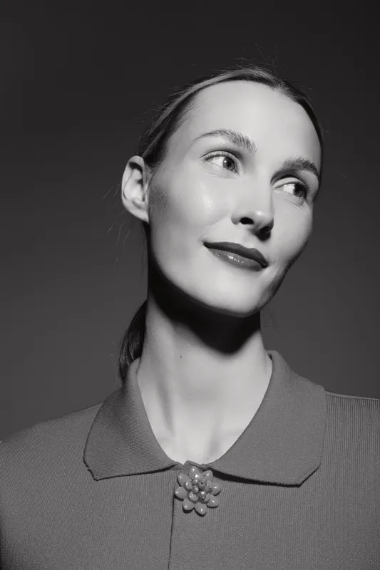Portrait of a fair skinned caucasian woman with slicked back hair and glossy lips looking aside. Studio lighting highlights facial features and textured collar. Concept of elegance and beauty.