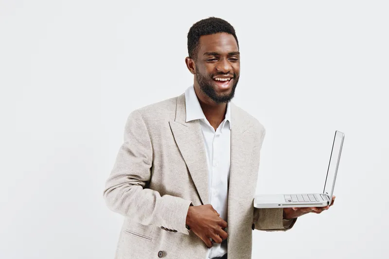 man smiling, young adult, casual beige blazer, white shirt, holding open laptop, white background, studio shot, technology, communication, business casual, happiness, success, professional