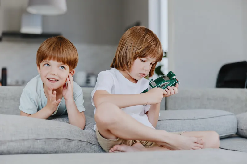 Two children playing together in a cozy living room, one boy focused on a toy car while the other observes, creating a joyful atmosphere of childhood fun.
