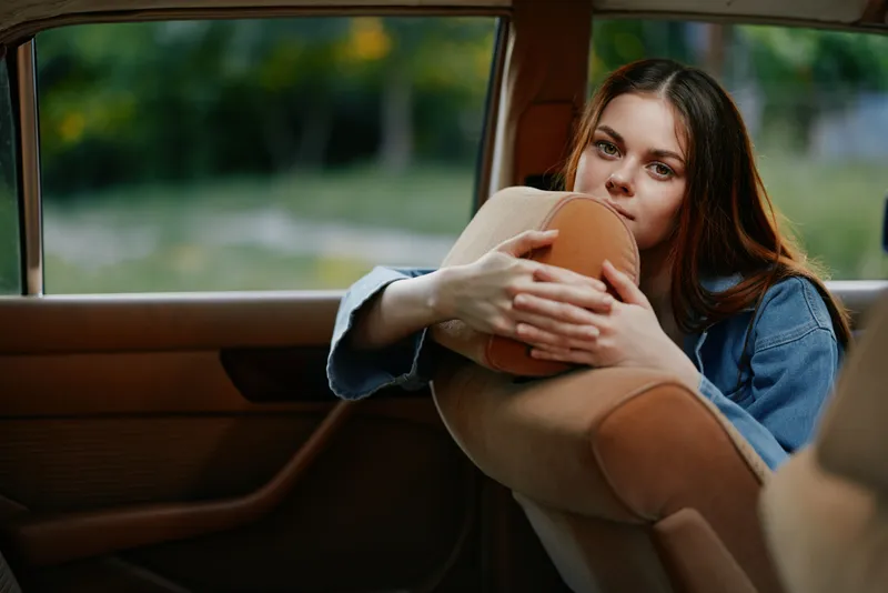 Thoughtful young woman resting in a car, reflecting on life, highlighting her emotions and serene atmosphere in natural light.