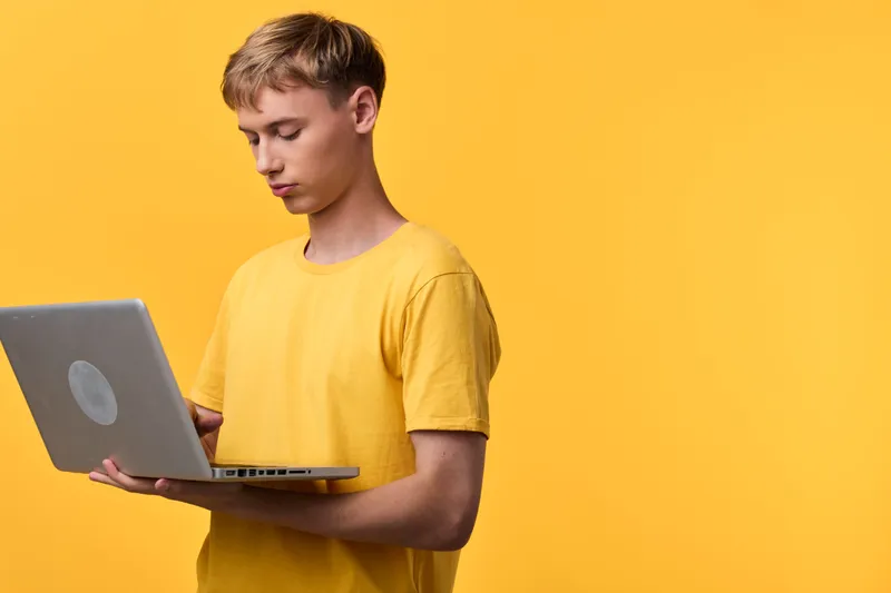 Young man in a yellow tee uses a laptop against a bright yellow backdrop, creating a modern tech workspace vibe for online learning or remote work
