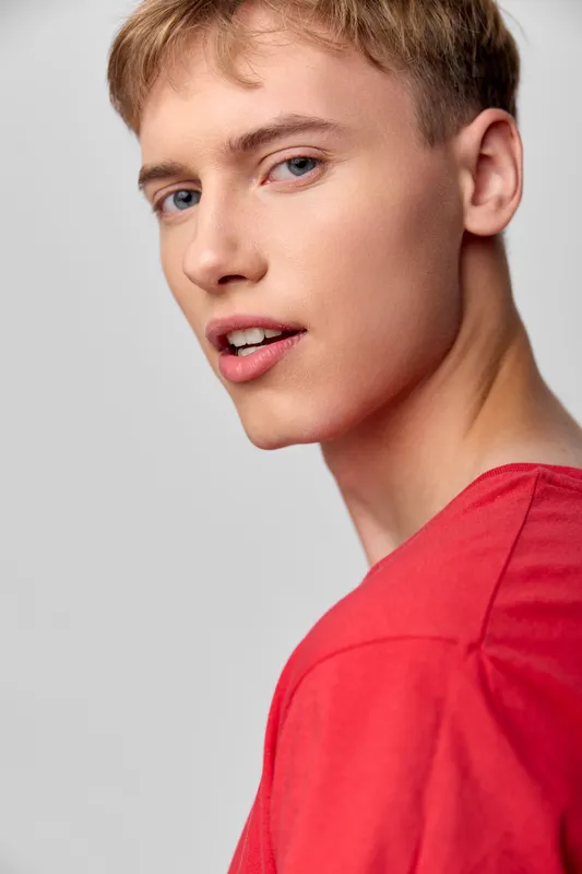 Young man with a red shirt looks over his shoulder in a clean studio setting, capturing modern casual style, confident gaze, and sharp lighting for fashion and stock creative use