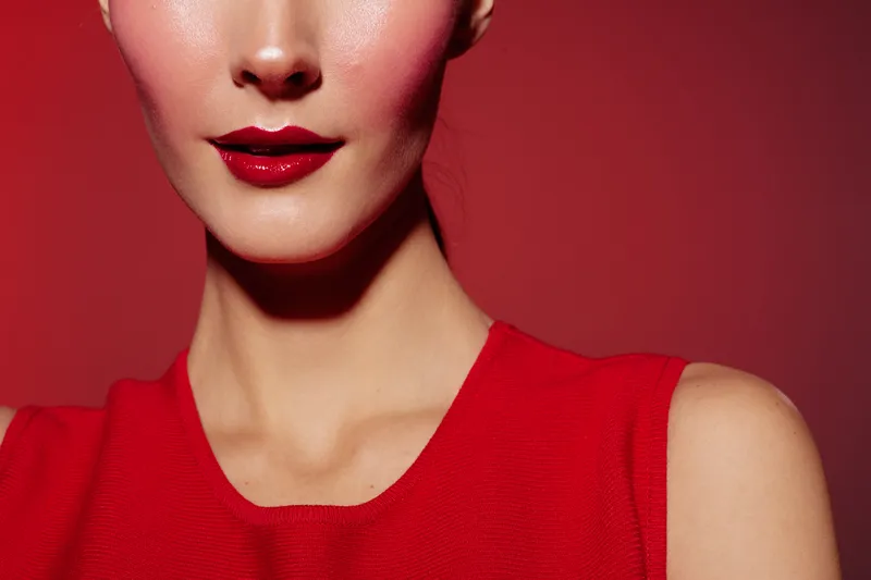 Close-up of a woman with red lipstick and red dress against a red background. The image highlights beauty, fashion, and makeup concepts with a bold and elegant style.