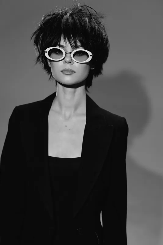 Black and white portrait of fashionable woman wearing sunglasses and blazer with short hair in studio lighting.