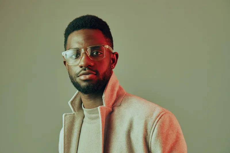 Stylish young man with glasses in a modern outfit, exuding confidence against a muted background, ideal for fashion and lifestyle concepts