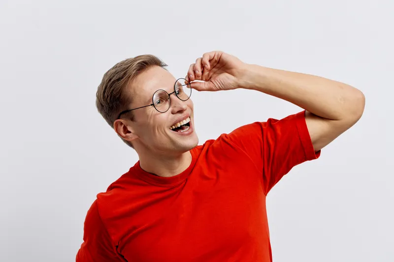Smiling young caucasian man in red t-shirt wearing round glasses looking aside happy joyful digital detox concept