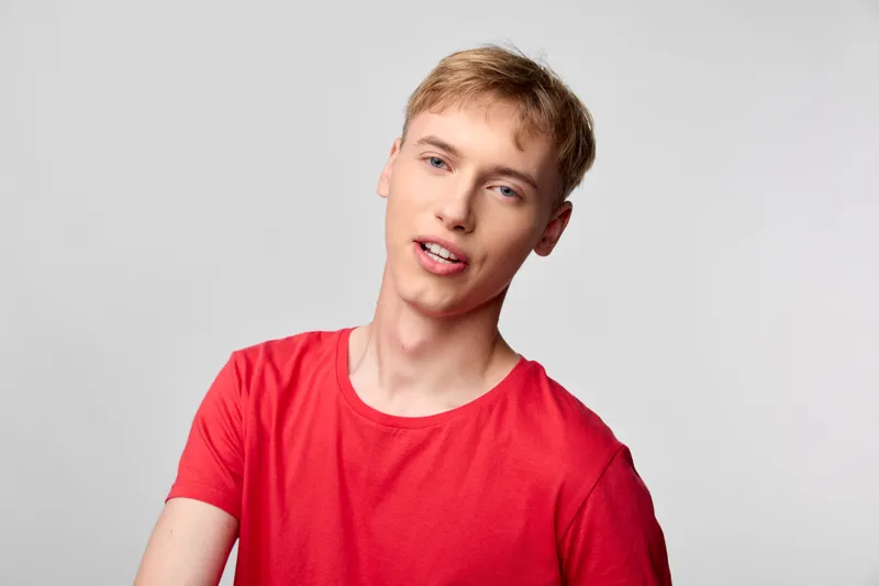 Young man in a red casual shirt stands in a bright studio with a neutral background, presenting a confident, relaxed expression ideal for lifestyle, fashion and product storytelling