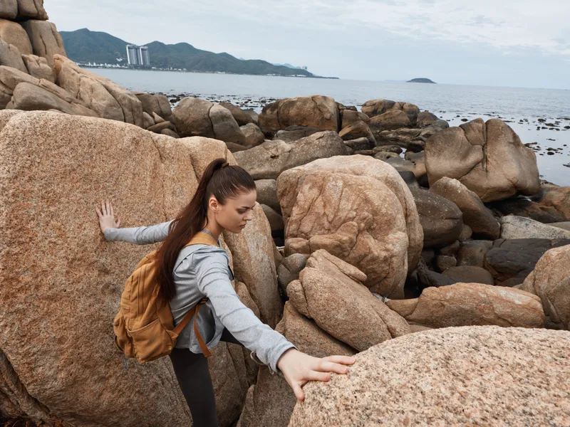 Young woman navigating rocky coastline, wearing casual outdoor clothing, showcasing determination amidst nature s splendor