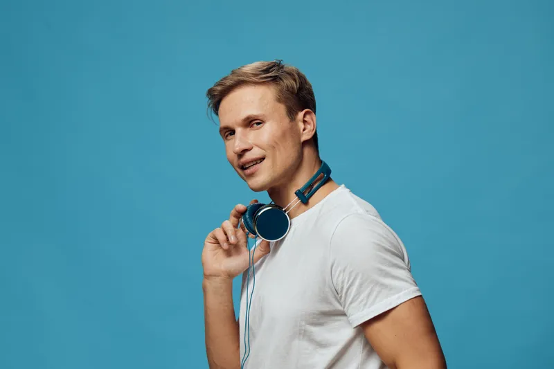 smiling young man wearing wireless headphones blue background casual white t-shirt digital detox relaxation concept