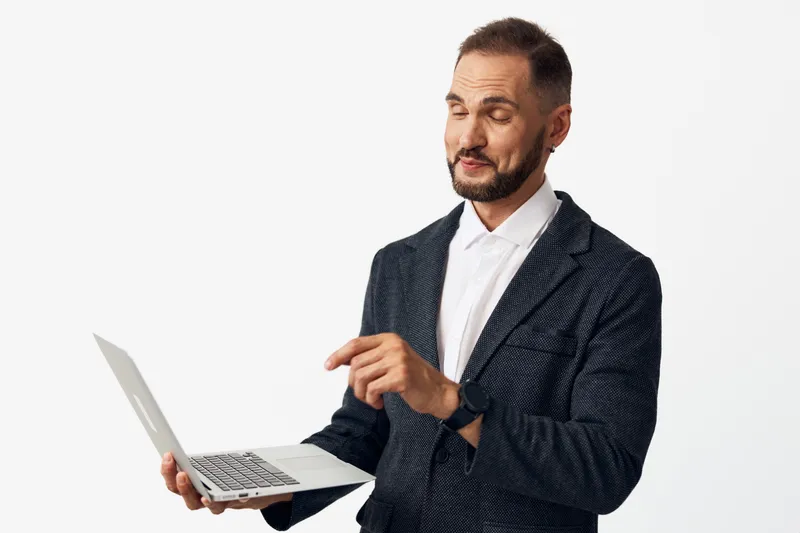 A professional man in a dark patterned blazer holds a laptop, projecting confidence, focus, and ambition against a clean isolated background.