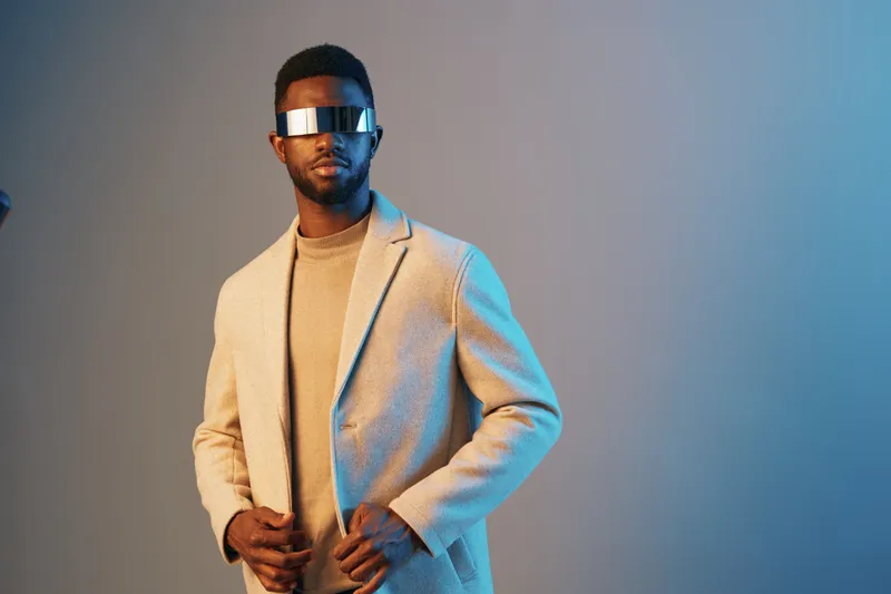 Stylish young man in a modern outfit and sunglasses against a blue background, exuding confidence and sophistication with a seasonal fashion vibe