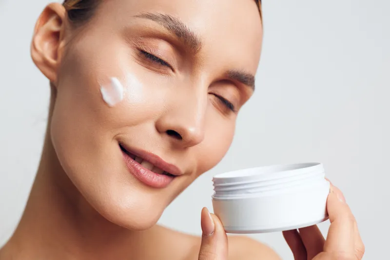 Woman skincare cream beauty jar face closeup cosmetic moisturizing moisturizer, young woman applies soft moisturizer on smooth skin, holding white jar, eyes closed, calm spa beauty routine on neutral