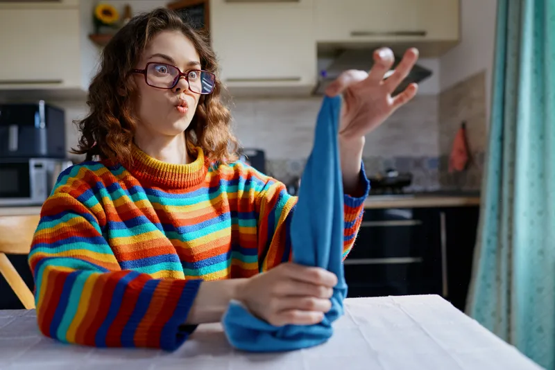 Woman with curly hair wearing a colorful striped sweater folds laundry in a bright kitchen, capturing daily lifestyle, home chores, and cozy domestic life.