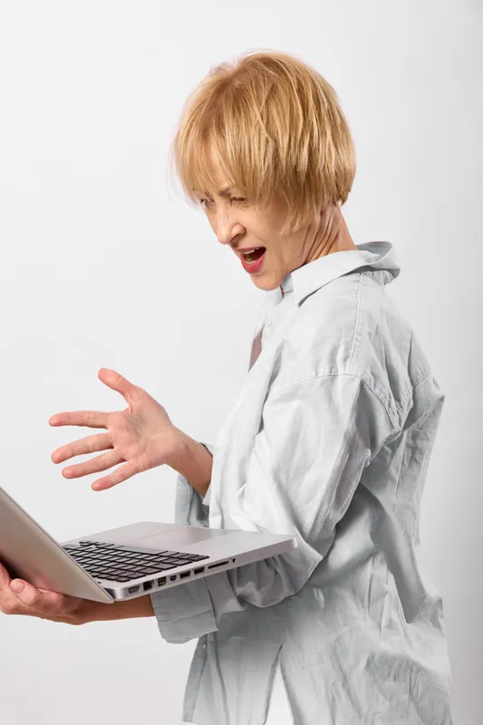 Woman with short hair holding a laptop, showing stress and illness and shocked expression. Studio portrait on white background, indoor office mood. Healthcare concept, headache anxiety.