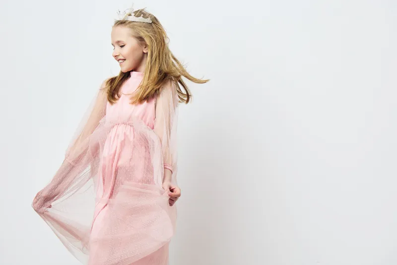 A joyful young girl in a pink tulle dress, twirling with a smile in front of a white background, embodying childhood happiness and playfulness