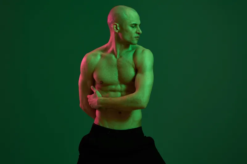Muscular man posing with strong body expression, showcasing fitness and determination against a vibrant green background. Ideal for health and sports themes.