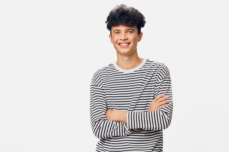 smiling young man in striped shirt with crossed arms, casual confident portrait, isolated white background, cheerful expression, curly hair style, relaxed pose