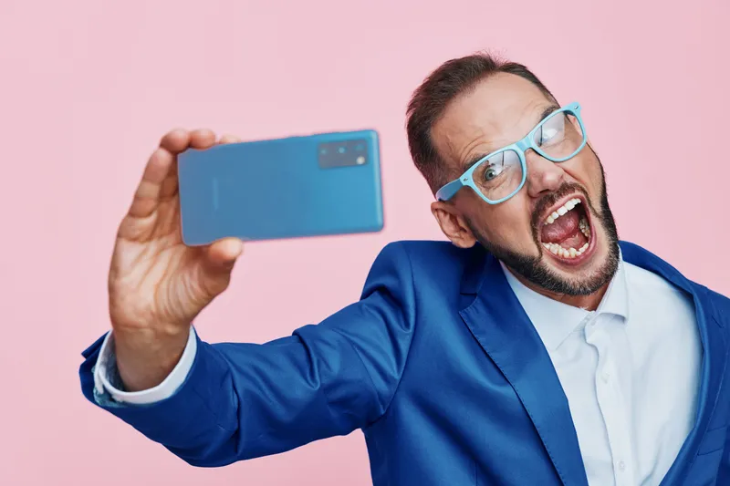 A confident business professional man on a vibrant pink background takes a selfie, showcasing bold emotion and a focused demeanor in a colorful isolated setting.