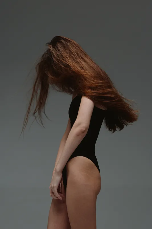 woman with long hair in black bodysuit posing on gray background with flowing hair