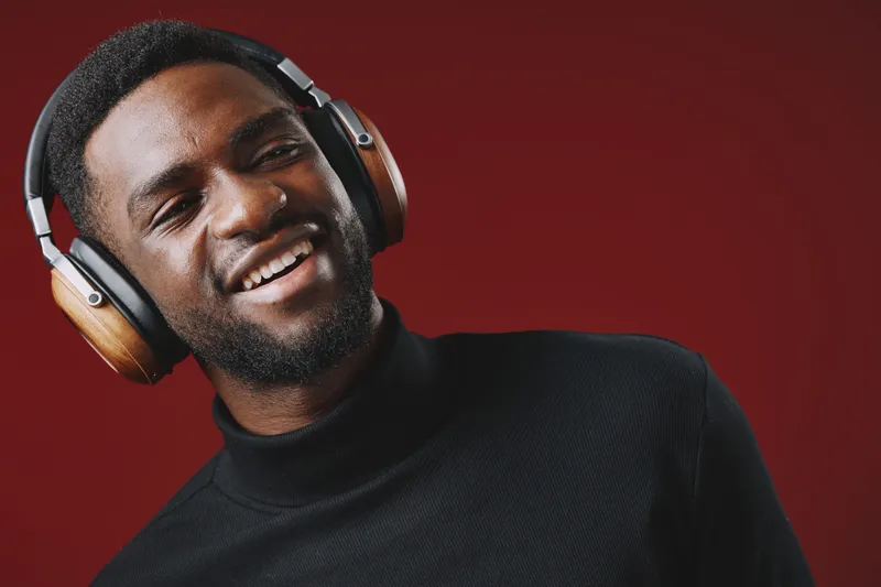 Smiling young Black man enjoying music with headphones against a red background, radiating positive emotions and modern style, perfect for music and lifestyle concepts