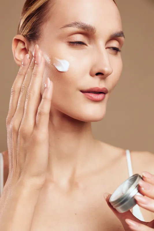 Young woman applying facial cream on clean skin with closed eyes, natural beauty concept, soft lighting, smooth texture, skincare routine, neutral background