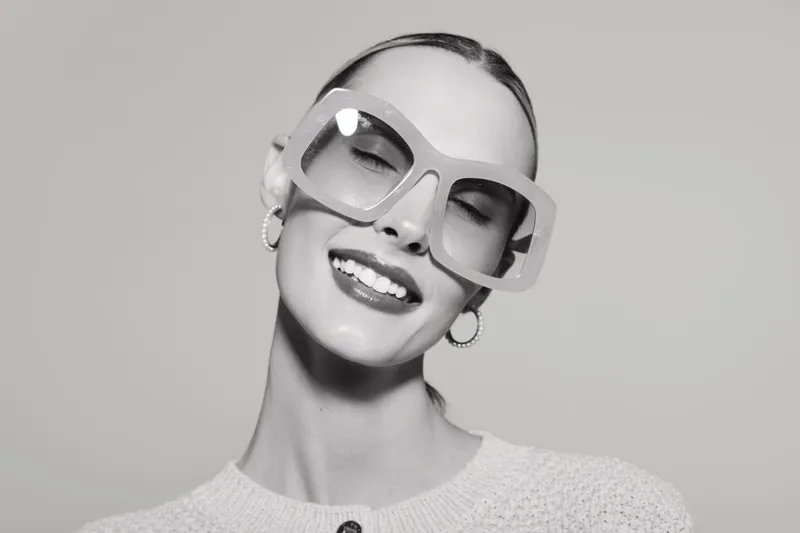 Smiling caucasian woman with fair skin and large glasses poses with closed eyes on grey background. Concept for fashion, eyewear, beauty, and joyful emotions.