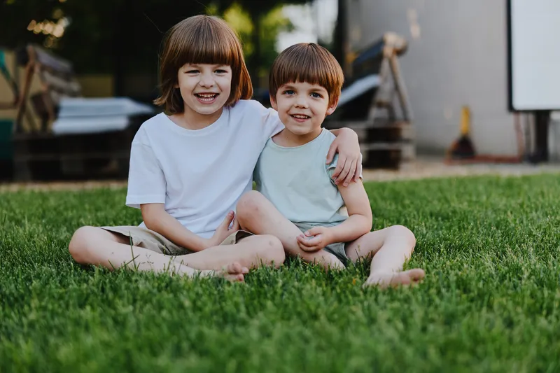 Two happy boys sitting on green grass, enjoying a sunny day outdoors. Their joyful expressions reflect the innocence and playfulness of childhood.