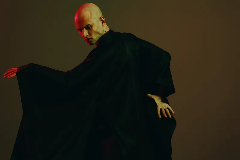 Male dancer in black robe showing elegance and artistry. Captivating movement and dramatic poses create a stunning visual impact, evoking a sense of mystery.