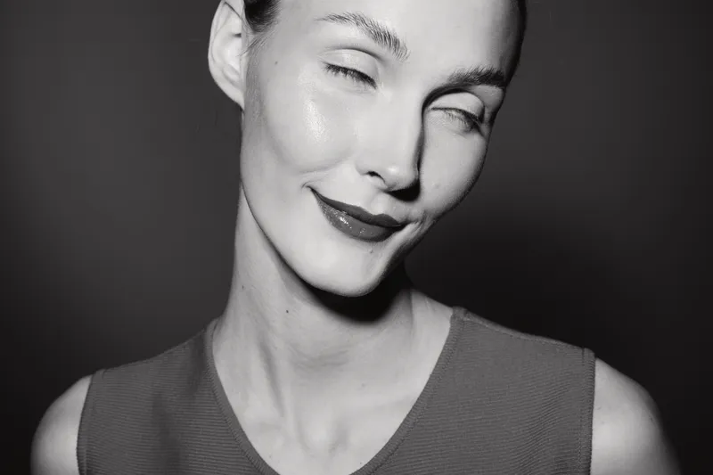 Portrait of a smiling white woman with light skin and slicked hair in a studio, expressing joy and confidence in black and white photography.